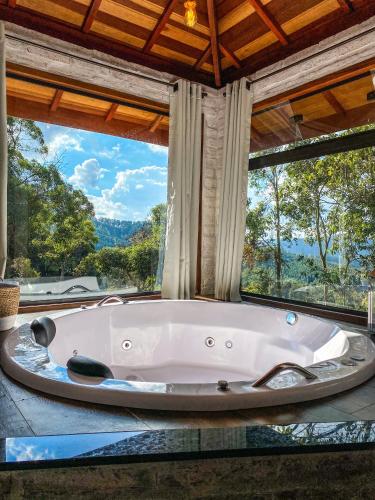 una vasca da bagno in una stanza con una grande finestra di Refúgio Physis Suítes a Monte Verde