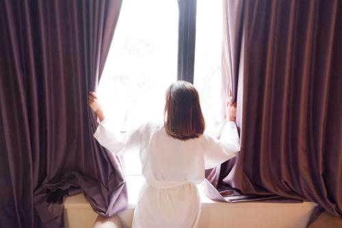 a woman in a white dress looking out of a window at News Hotel Waru Sidoarjo in Waru