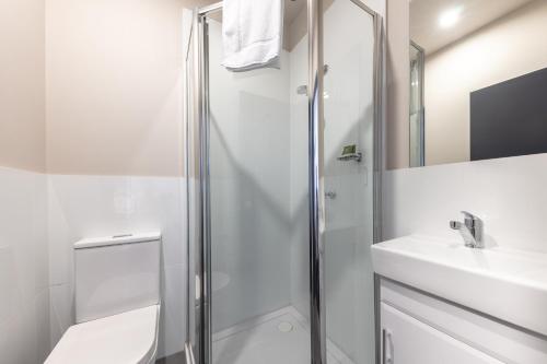 baño blanco con ducha y lavamanos en Lakemba Hotel en Sídney