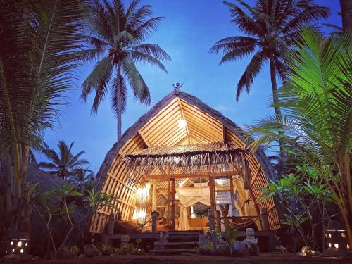 une maison en bambou avec des palmiers en arrière-plan dans l'établissement Coconut Garden Beach Resort, à Maumere