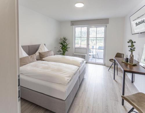 a white bedroom with a bed and a desk and a window at Pension Talblick in Sulz am Neckar