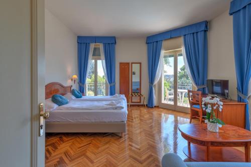 a bedroom with a bed with blue curtains and a table at Hotel Galeazzi in Gardone Riviera