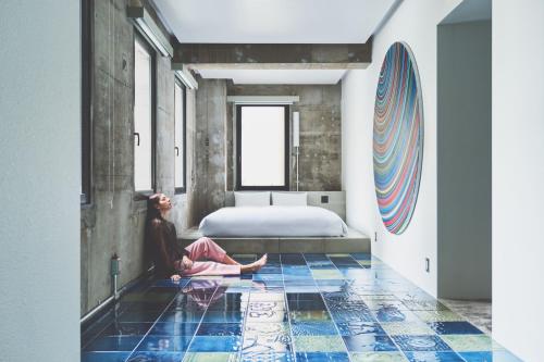 a woman sitting on the floor in a room with a bed at BnA WALL in Tokyo