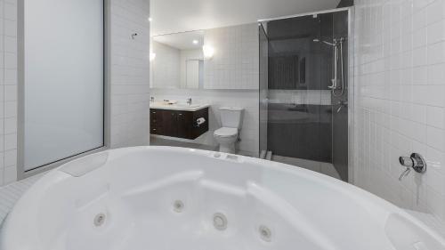 a white bathroom with a tub and a toilet at Oaks Adelaide Embassy Suites in Adelaide