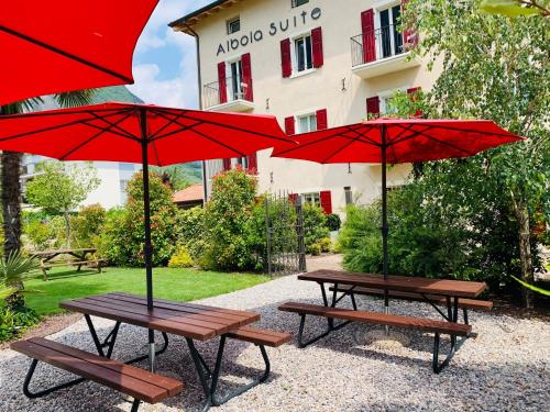 two picnic tables with red umbrellas in front of a building at Albola Suite Holiday Apartments in Riva del Garda