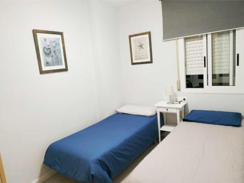 a bedroom with two beds and a nightstand and a window at APARTAMENTO EN EL CENTRO DE CALAFELL in Calafell