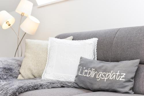 eine graue Couch mit einem Kissen mit der Beleuchtungseinrichtung in der Unterkunft Ferienhaus Windspiel in Neuharlingersiel