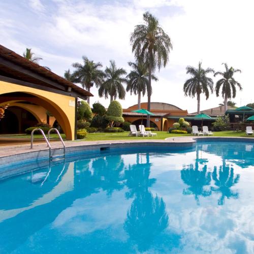 a large swimming pool with palm trees in the background at Hotel & Motel Hacienda Jiutepec in Jiutepec
