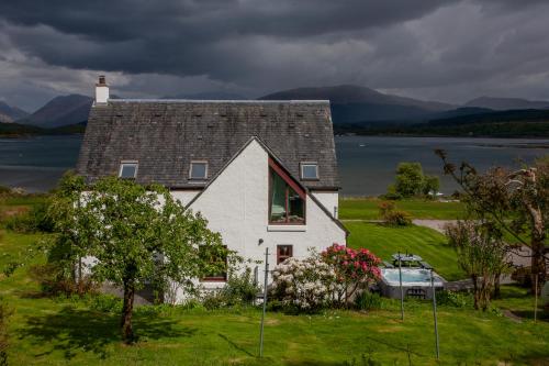 a white house on a hill with a boat in front of it at Seabank Lochside Farmhouse in Oban