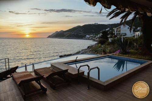 a swimming pool next to the ocean at sunset at Resort Stikovic in Dobra Voda