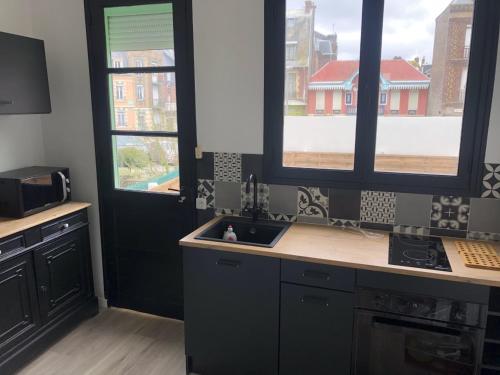 een keuken met een wastafel en 2 grote ramen bij Villa les Fleurs Appartement en front de mer in Mers-les-Bains