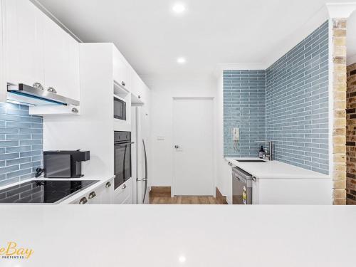 a kitchen with white cabinets and a blue tile wall at Bay Parklands Unit 70 in Nelson Bay