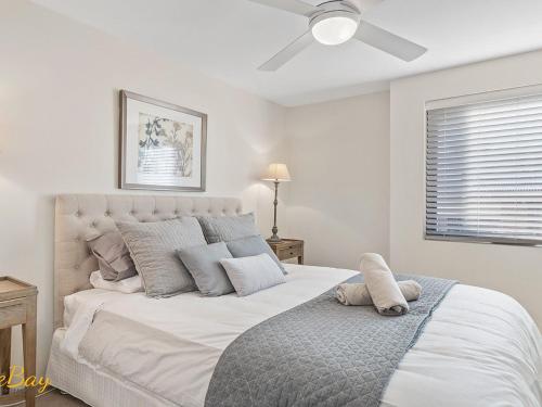 a white bedroom with a bed with a ceiling fan at Wanda Beach Unit 2 Soldiers Point Road in Salamander Bay