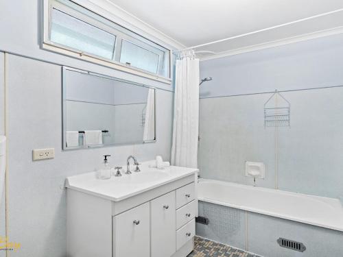 a white bathroom with a sink and a tub and a window at Lentara Street No 31 in Fingal Bay