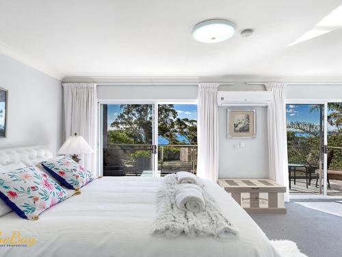 a white bedroom with a large white bed and windows at Water Views on Wallawa in Nelson Bay