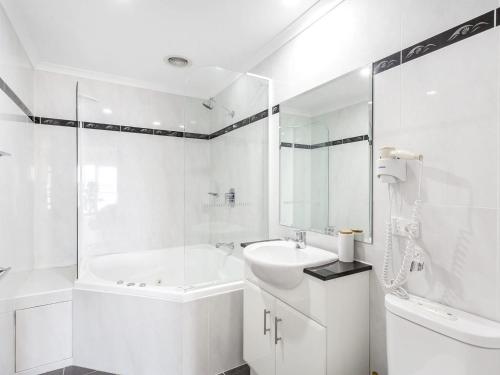 Baño blanco con bañera y lavamanos en Breakwater Apartment 403, en Shoal Bay