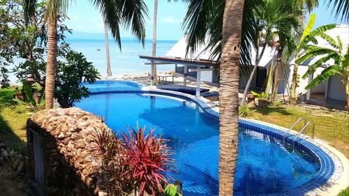 a swimming pool with a palm tree next to the ocean at Islandlife Bungalows in Thongsala