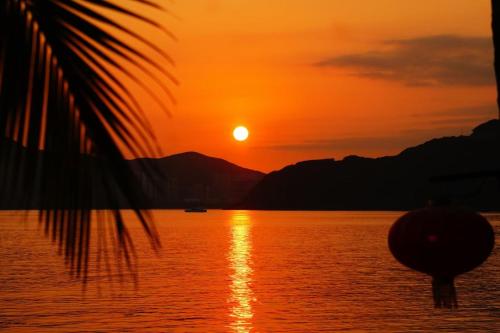 a sunset over a body of water with a palm tree at Mandarin Oriental, Sanya in Sanya