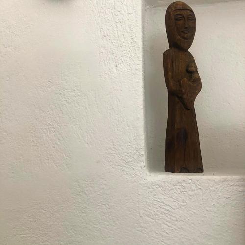 a wooden statue of a person hanging on a wall at Thera Incognita Studios in Perissa