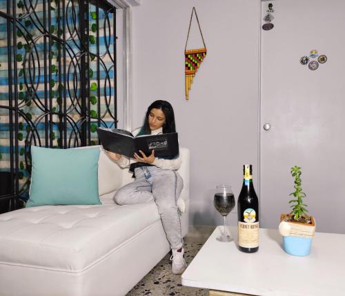 a woman sitting on a couch reading a book at KEY WEST HOSTEL in Medellín