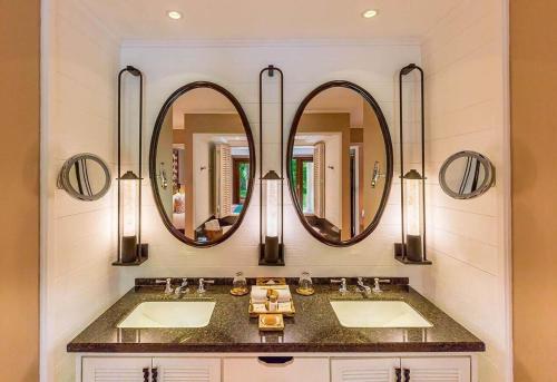 a bathroom with two sinks and two mirrors at Constance Lemuria in Grand'Anse Praslin