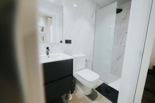 a white bathroom with a toilet and a sink at Apartamentos MK77 León - Palomera in León