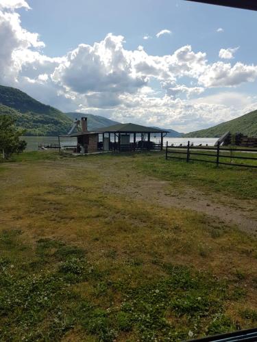 a building in a field next to a body of water at Pensiunea Lorena in Cozla