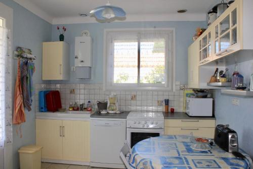 une cuisine avec des armoires blanches et une table à l'intérieur dans l'établissement Maison de famille à St Hilaire de Riez, à Saint-Hilaire-de-Riez