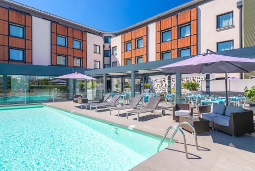 einen Pool mit Stühlen und Sonnenschirmen neben einem Gebäude in der Unterkunft Holiday Inn Toulouse Airport, an IHG Hotel in Blagnac