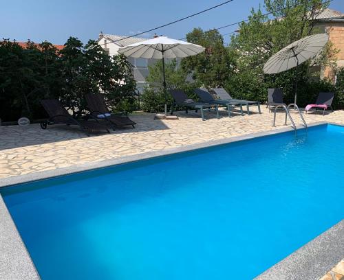 a blue swimming pool with chairs and umbrellas at Apartments Ban in Novi Vinodolski