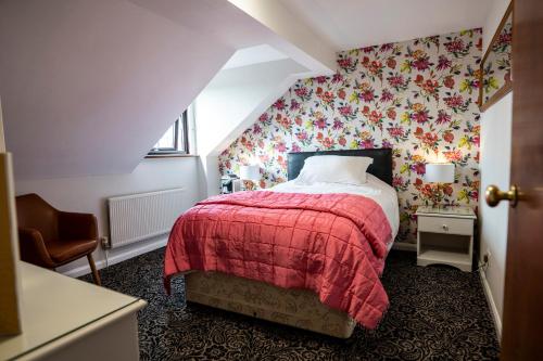 1 dormitorio con cama roja y papel pintado con motivos florales en Quilt and Croissants Guest House, en Stratford-upon-Avon