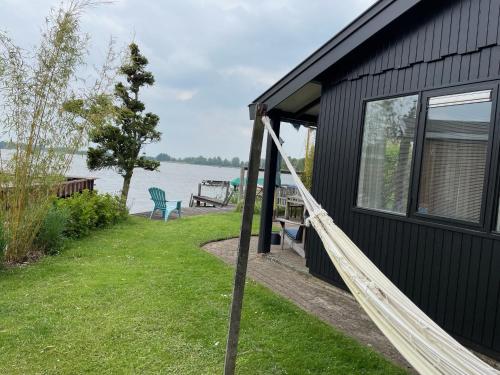 a black house with a porch next to the water at The Outpost Lakehouse- enjoy our house at Reeuwijkse Plassen - near Gouda in Reeuwijk