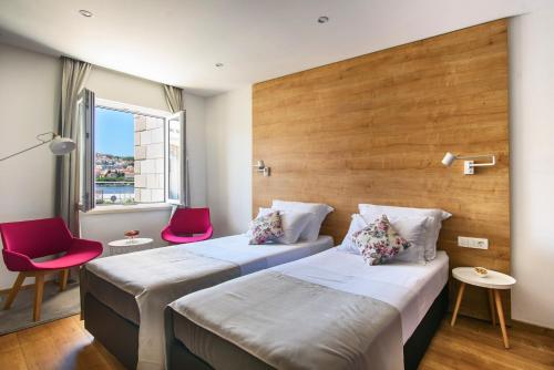 two beds in a hotel room with two pink chairs at Ora Luxury Rooms in Dubrovnik