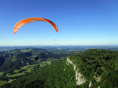 une personne en parachute survolant une montagne dans l'établissement Domaine de Bellevue Gîte du Mont Poupet, à Marnoz