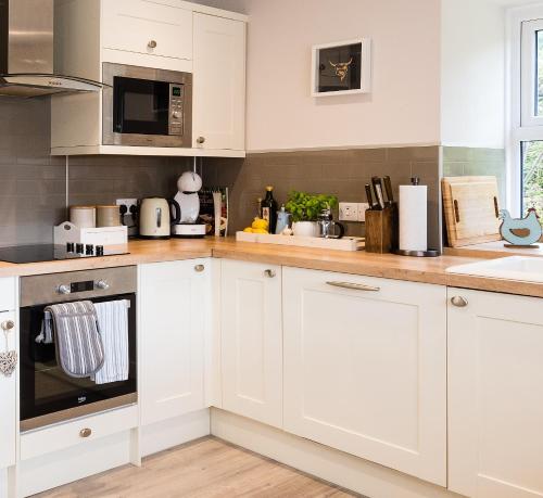 a white kitchen with white cabinets and appliances at Smithy Cottage in Kirkmichael
