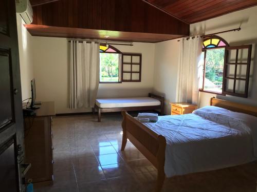a bedroom with a bed and a bench and two windows at Pousada Acacia Imperial in Aldeia Velha