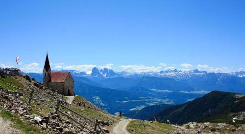 a church on the side of a hill with mountains at Teutenhofer Kirsche in Feldthurns