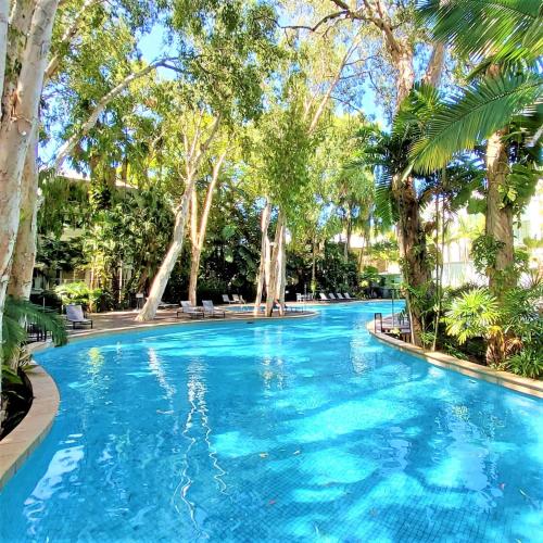 a swimming pool with blue water and trees at Palm Cove Beach Apartment in Palm Cove