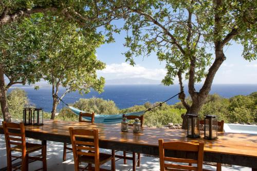 a table with chairs and a hammock overlooking the ocean at My Old Stone House in a 2 000 sqm private garden with Fab Glamping Tent in Mandrakion