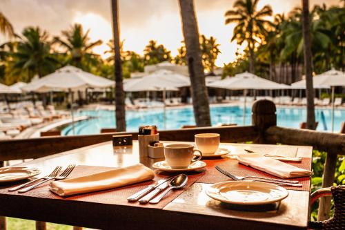 a table with coffee cups and utensils and a pool at Shandrani Beachcomber Resort & Spa in Blue Bay