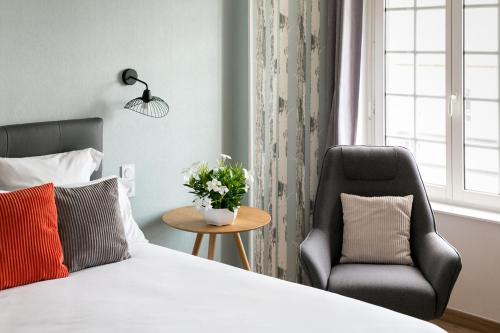 a bedroom with a bed and a chair at Le Cotentin Appart'hôtels & Restaurant le Cot' in Portbail