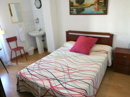 um quarto com uma cama com uma almofada vermelha e um lavatório em Pension Carretero em Cáceres