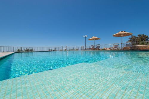 a large swimming pool with blue water and umbrellas at Castello Bonaria Wine & Spa Resort in Campiglia Marittima