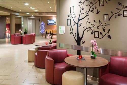 a waiting room with red chairs and a tree on the wall at Campanile Toulouse Purpan in Toulouse