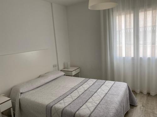 a white bedroom with a bed and a window at VicAm Atico Duplex in Pineda de Mar