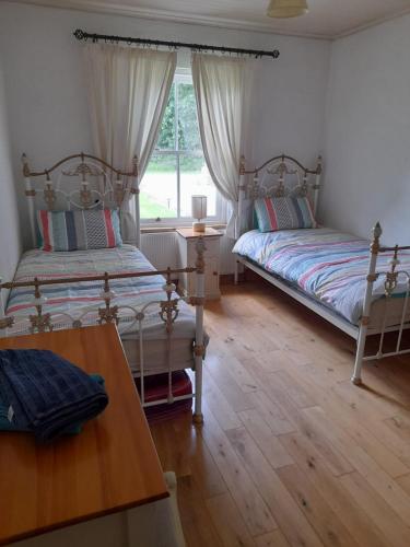 a bedroom with two beds and a table and a window at Katy Kellys Countryside Self Catering Cottage in Roscommon