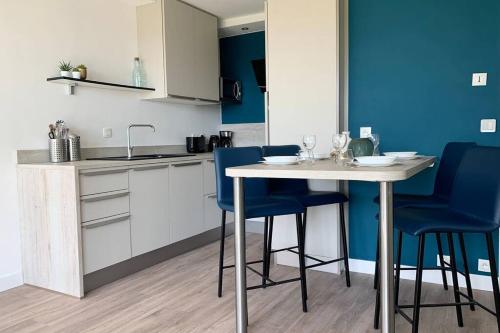 une cuisine avec une table blanche et des chaises bleues dans l'établissement Le Charmant, appartement situé dans la résidence de standing, les Dunes du Golf à Wimereux, à Wimereux