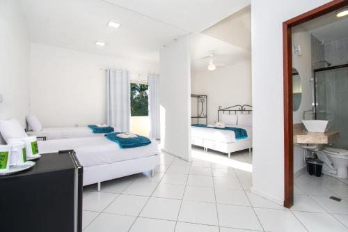 a white room with two beds and a bathroom at Pousada Casuarina Ferradura in Búzios