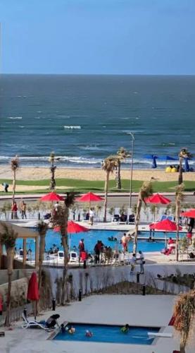 a beach with a swimming pool with palm trees and red umbrellas at Porto Said in Port Said