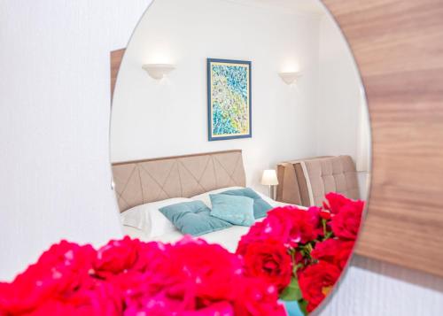 a bedroom with a bed and red flowers in a mirror at Guest House Medin in Petrovac na Moru